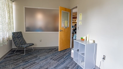 A well-lit open room with shelves, chairs and a wide-screen monitor