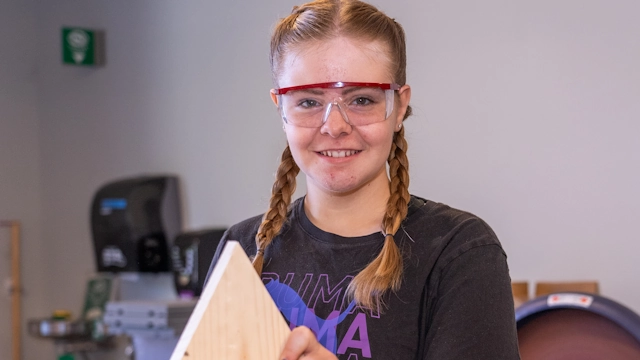 A girl in goggles building a birdhouse